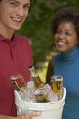 Mann hält Eiskübel mit Bierflaschen, Frau im Hintergrund