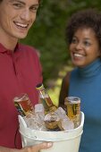 Man holding ice bucket full of beer bottles, woman in background