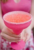 Frau hält pinkfarbenes Glas mit Cocktail