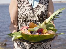 Frau hält Tablett mit frischen exotischen Früchten am Meer