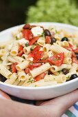 Hand holding a dish of pasta and vegetable salad