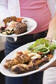 Two people holding plates of grilled food (different)