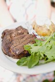 Woman holding plate of grilled steak, baked potato & salad