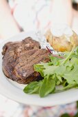 Frau hält Teller mit Grillsteak, Baked Potatoe und Blattsalat