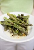 Person holding a plate of grilled green asparagus