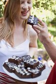 Man's hand offering woman a brownie at a garden party