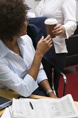 Hand passing cup of coffee to woman in office