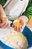 Kind gibt aufgeschlagenes Ei zu Mehl und Butter in Schüssel