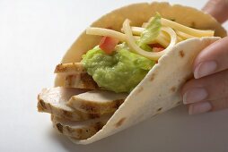 Hand holding folded tortilla filled with chicken, guacamole, cheese
