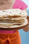 Frau hält frisch gebackene Tortillas auf Tablett