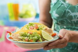 Frau hält Teller mit zwei Hähnchen-Tacos