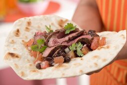 Woman holding fajita with beef, beans and tomatoes