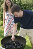 Paar grillt im Garten (Mann zündet Holzkohle an)