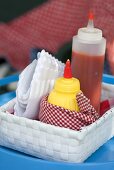 Ketchupflasche, Senf und Papierservietten im Korb