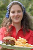 Frau hält Teller mit Hamburger und Pommes frites