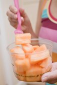 Woman eating diced melon out of plastic tub
