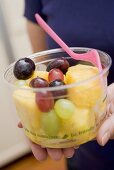 Woman holding plastic tub of fruit salad with fork
