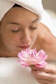 Woman lying on white towel, smelling flower