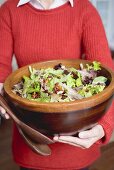Woman holding large bowl of salad leaves with nuts