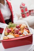 Roasted root vegetables in roasting dish, woman in background