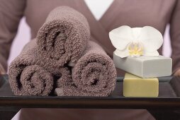 Woman holding towels, soaps and orchid on tray