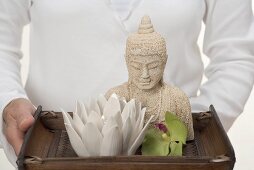 Frau hält Tablett mit Buddhastatue, Kerze und Orchidee