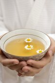 Hands holding bowl of chamomile tea with flowers