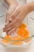 Frau wäscht ihre Hände in Seifenwasser mit Ringelblumen