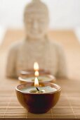 Three tea lights on bamboo mat in front of Buddha statue