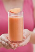 Woman holding glass of mango smoothie with wedge of mango