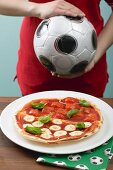 Tomaten-Mozzarella-Pizza, Fussballspielerin im Hintergrund