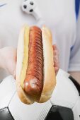 Footballer holding hot dog with mustard