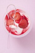 Strawberry yoghurt in plastic pot with spoon (overhead view)