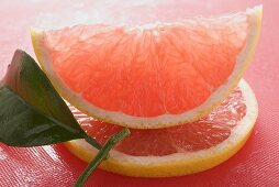 Wedge of pink grapefruit on slice of grapefruit with leaf