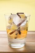 Rum and ice cubes with spices and pieces of fruit in glass