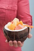 Woman holding hollowed-out coconut full of exotic fruit salad