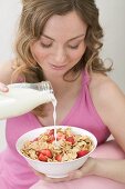 Frau giesst Milch auf Cornflakes mit Erdbeeren