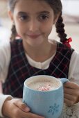 Girl holding large mug of cocoa with pieces of candy cane