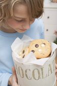 Boy looking at chocolate chip cookies in cookie tin