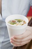 Frau hält Pappbecher mit asiatischer Nudelsuppe