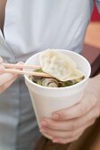 Frau hält Pappbecher mit asiatischer Nudelsuppe