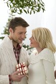 Mann überreicht Frau Weihnachtsgeschenk unter Mistelzweig
