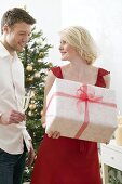 Woman holding large Christmas parcel, man holding glass of wine