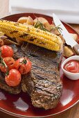 Grilled steak, corn on the cob, cherry tomatoes, potatoes, ketchup