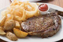 Rib-eye steak with onion rings, ketchup and potato wedges