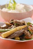 Beef with vegetables & sesame seeds, rice in background (Asia)