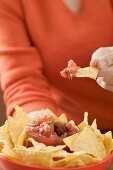 Frau hält Nachos mit Tomatensalsa