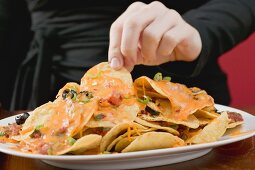 Hand reaching for tortilla chips with melted cheese