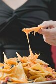 Hand taking tortilla chip with melted cheese from plate