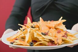 Frau hält Teller mit überbackenen Nachos